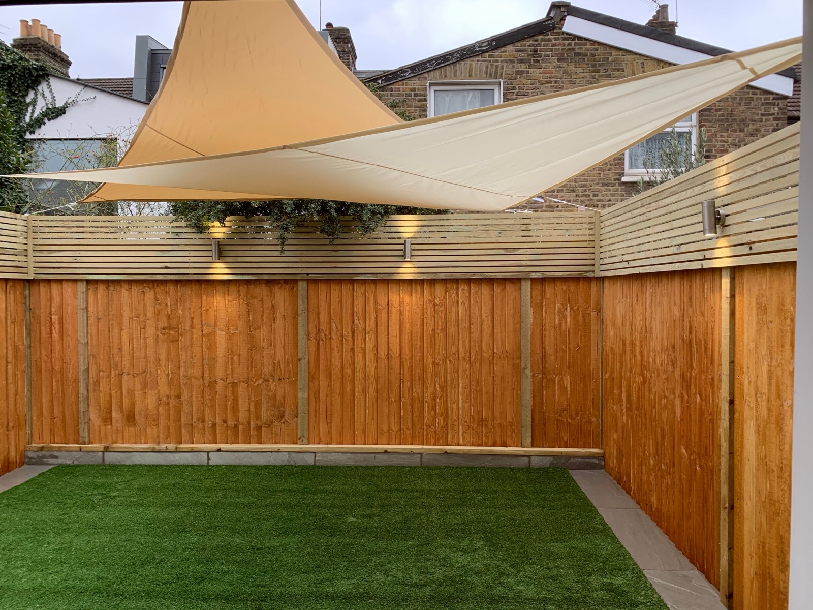 Garden with sail shade canopy, timber fencing and artificial lawn